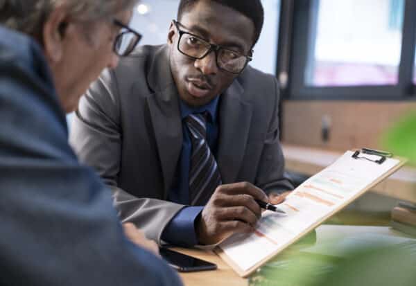 Two professionals review a clipboard with a resume or report, one guiding with a pen in a business discussion at a desk