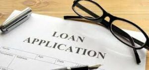 Close-up of a loan application form on a wooden desk, with a pen, a pair of black glasses, and a stapler.