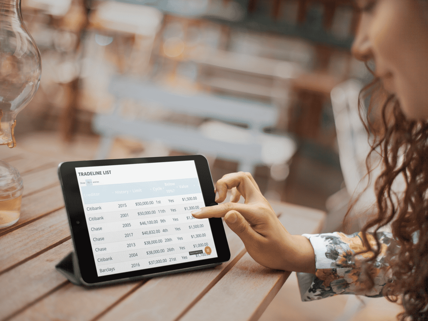 Person using a tablet on a wooden table, showing a spreadsheet titled 'TRADELINE LIST' with banks and financial data